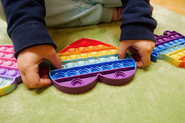 Kind hat ein herzförmiges Spielzeug in Regenbogenfarben. Es lässt die Erhebungen darin „ploppen“.