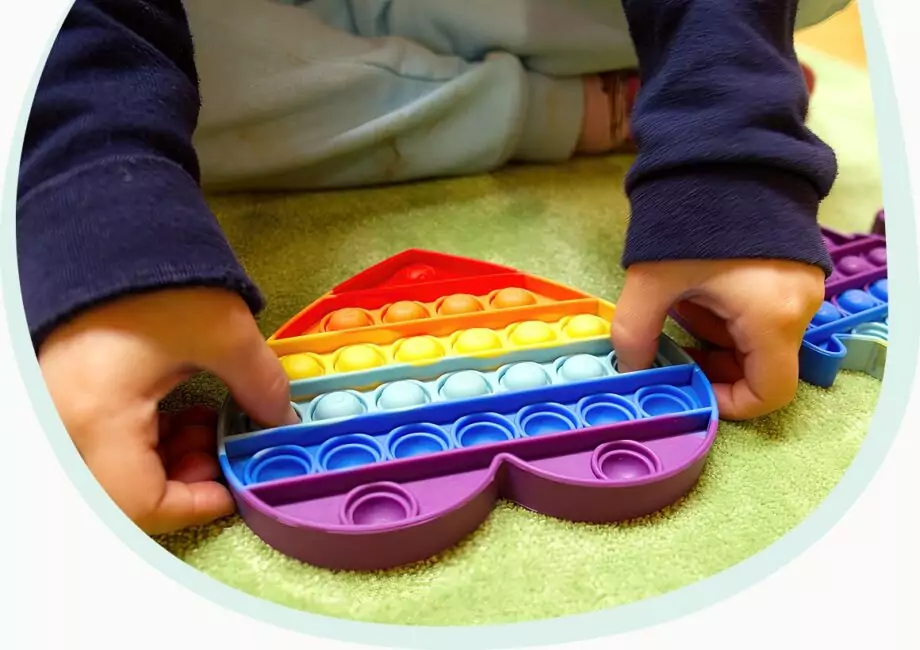 Kind hat ein herzförmiges Spielzeug in Regenbogenfarben. Es lässt die Erhebungen darin „ploppen“.